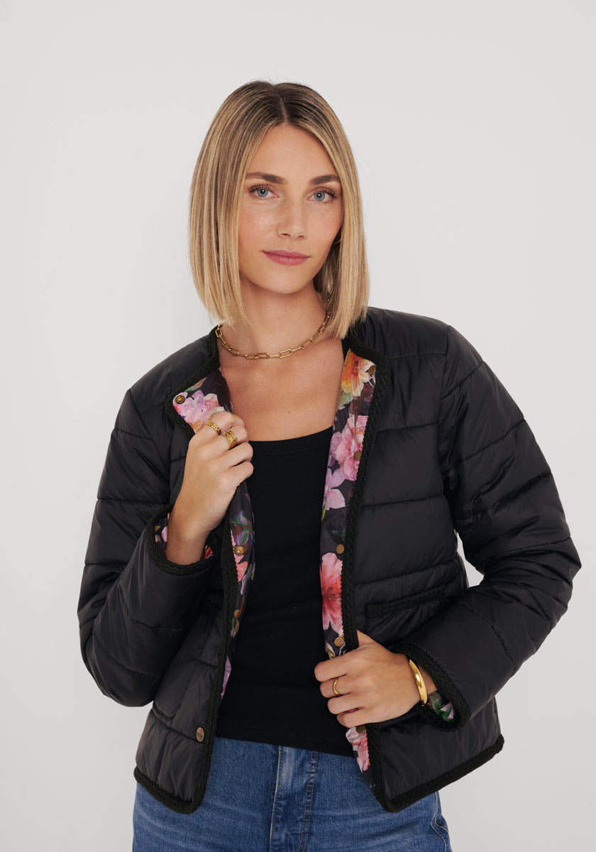 Eine Frau mit glattem blondem Haar modelliert eine Princess Goes Hollywood gesteppte Kurzjacke mit geblümtem Futter, ein schwarzes Rundhalsausschnitt-Top und blaue Jeans, die mit Goldschmuck vor einem weißen Hintergrund verziert sind.