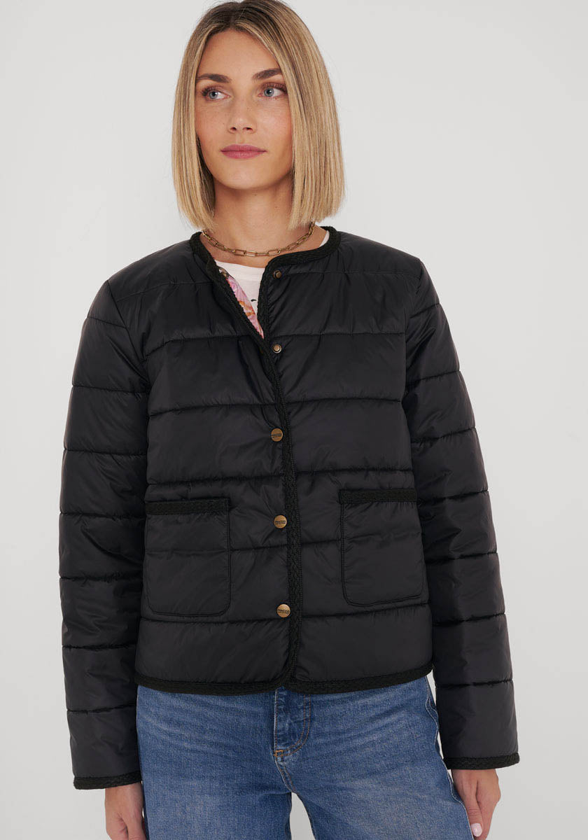 Eine Frau mit glattem, schulterlangem blondem Haar trägt eine schwarze gesteppte Kurzjacke mit Rundhalsausschnitt und goldenen Knöpfen von Princess Goes Hollywood. Sie steht vor weißem Hintergrund, trägt blaue Jeans und ein florales Top am Ausschnitt.