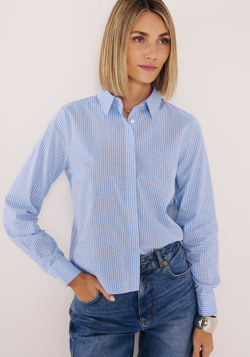 Eine Frau mit glattem, schulterlangem blondem Haar trägt eine hellblau-weiß karierte Bluse von Princess Goes Hollywood und blaue Jeans. Sie steht vor einem cremefarbenen Hintergrund und blickt mit einem entspannten Lächeln leicht zur Seite.