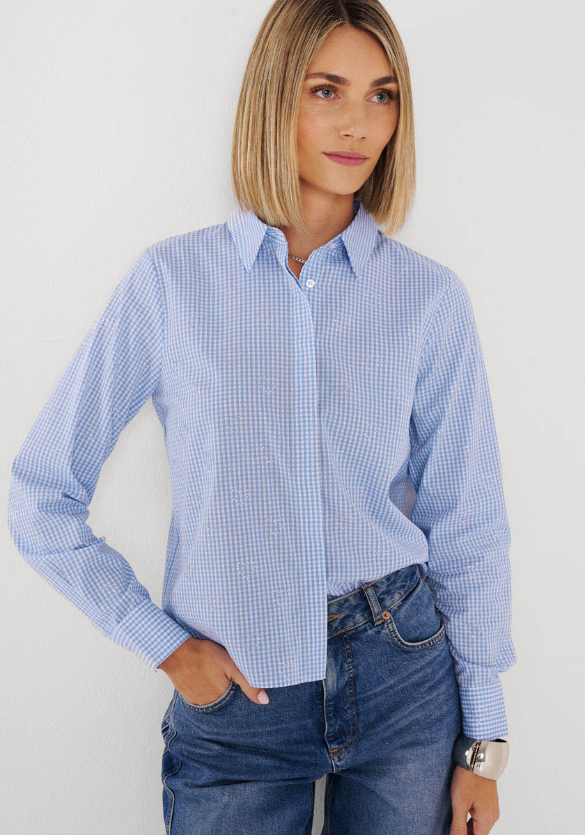 Eine Frau mit glattem blondem Haar trägt ein Princess Goes Hollywood Vichy-Karo-Baumwollhemd, das in eine blaue Jeans gesteckt ist. Sie steht vor einem weißen Hintergrund, eine Hand in der Tasche, blickt leicht zur Seite und lächelt sanft.