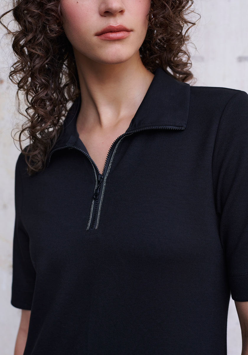 A woman with curly brown hair wears a black Princess Goes Hollywood Mini Sweatkleid with a collared neckline and partially unzipped zipper. Her lips and jawline are partly visible against a light, textured wall background.
