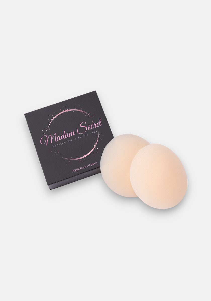 A pair of round, beige selbstklebend Silikon Nipple Covers by Princess Goes Hollywood rests beside a black Madam Secret package with pink cursive text, sparkles, and extra details on a plain white background.