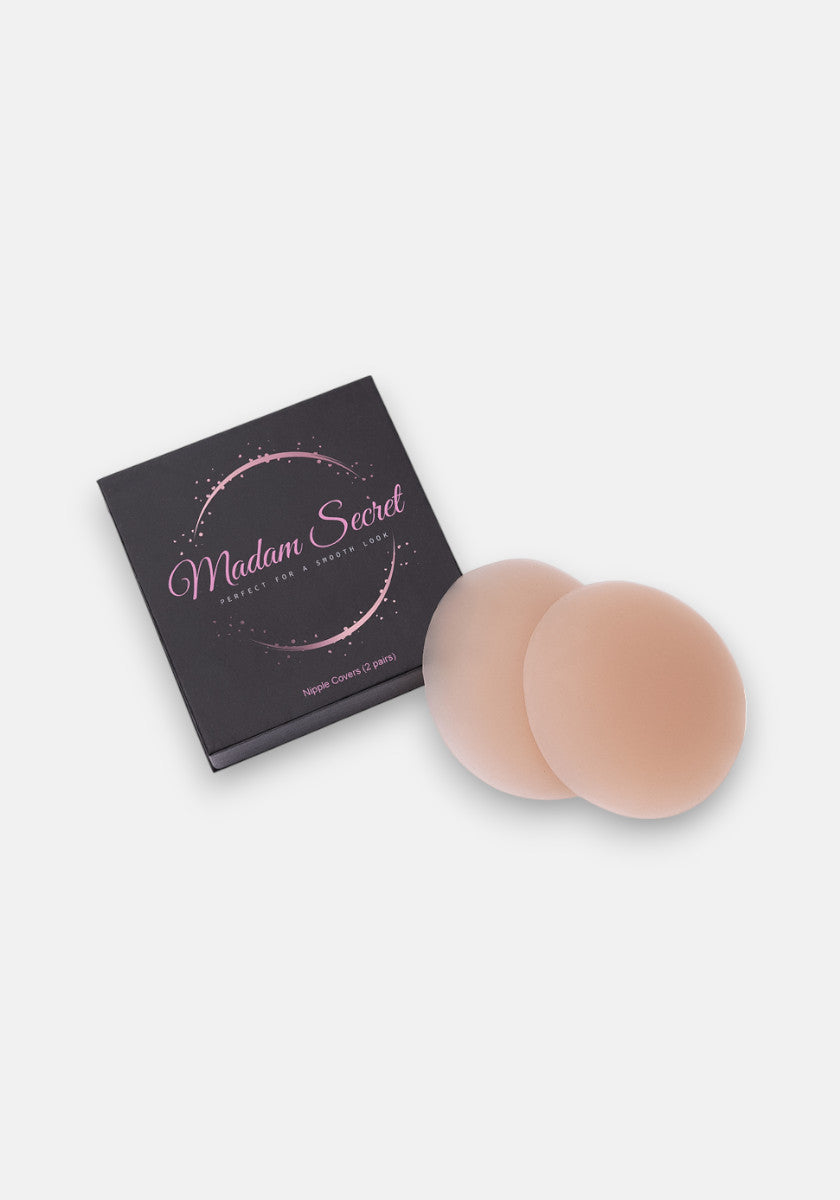 A pair of round, beige Princess Goes Hollywood Silikon Nipple Covers liegt neben einer schwarzen Box mit pinkem Aufdruck; die selbstklebenden Produkte sind auf weißem Hintergrund arrangiert.