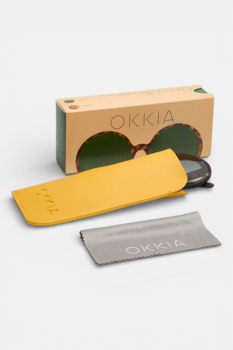 Ein Paar Okkia Schildpatt Oversize Sonnenbrillen, teilweise in einem gelben OKKIA-Etui, mit einem grauen OKKIA-Putztuch und einer beigen Damen Sonnenbrillen-Box, alles auf weißem Hintergrund.