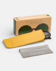 Ein Paar Okkia Schildpatt Oversize Sonnenbrillen, teilweise in einem gelben OKKIA-Etui, mit einem grauen OKKIA-Putztuch und einer beigen Damen Sonnenbrillen-Box, alles auf weißem Hintergrund.