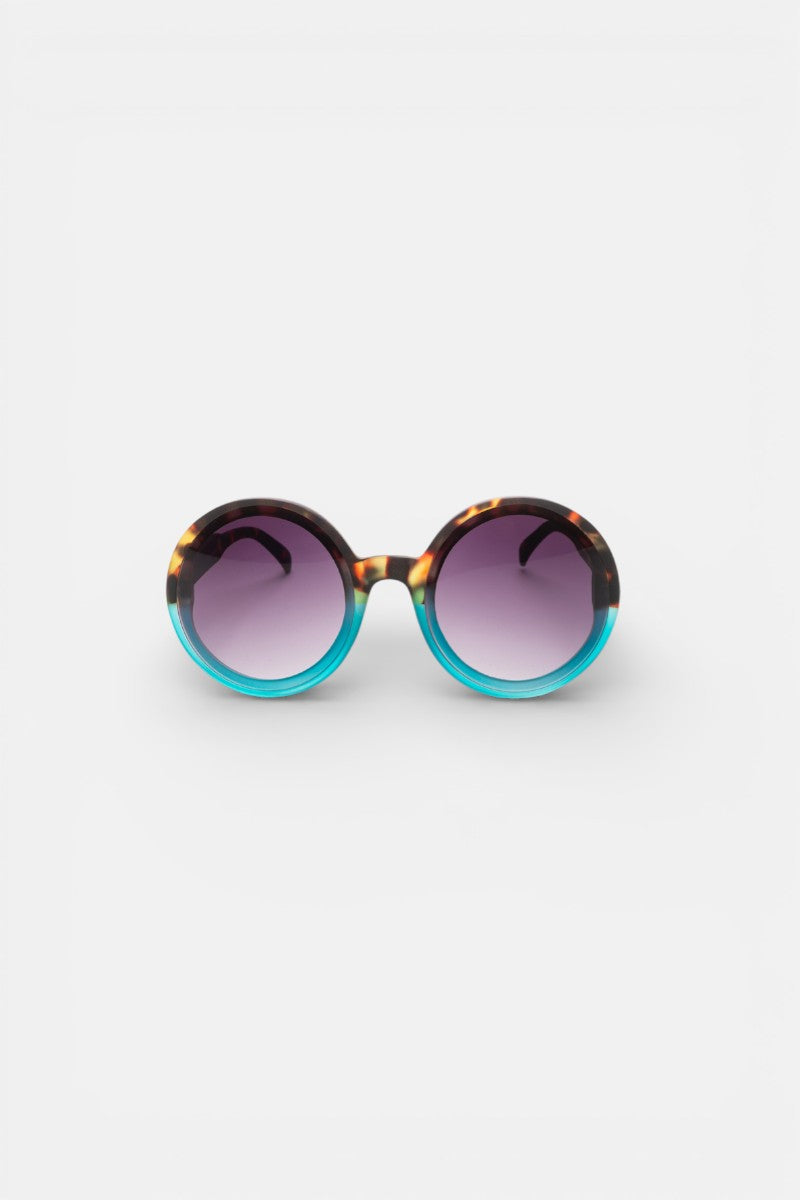 Okkia Oversize-Sonnenbrille mit runder, dicker Fassung: oben Tortoiseshell-Muster, unten leuchtendes Türkisblau. Violett getönte Gläser mit UV 400 Schutz. Präsentiert auf weißem Hintergrund.