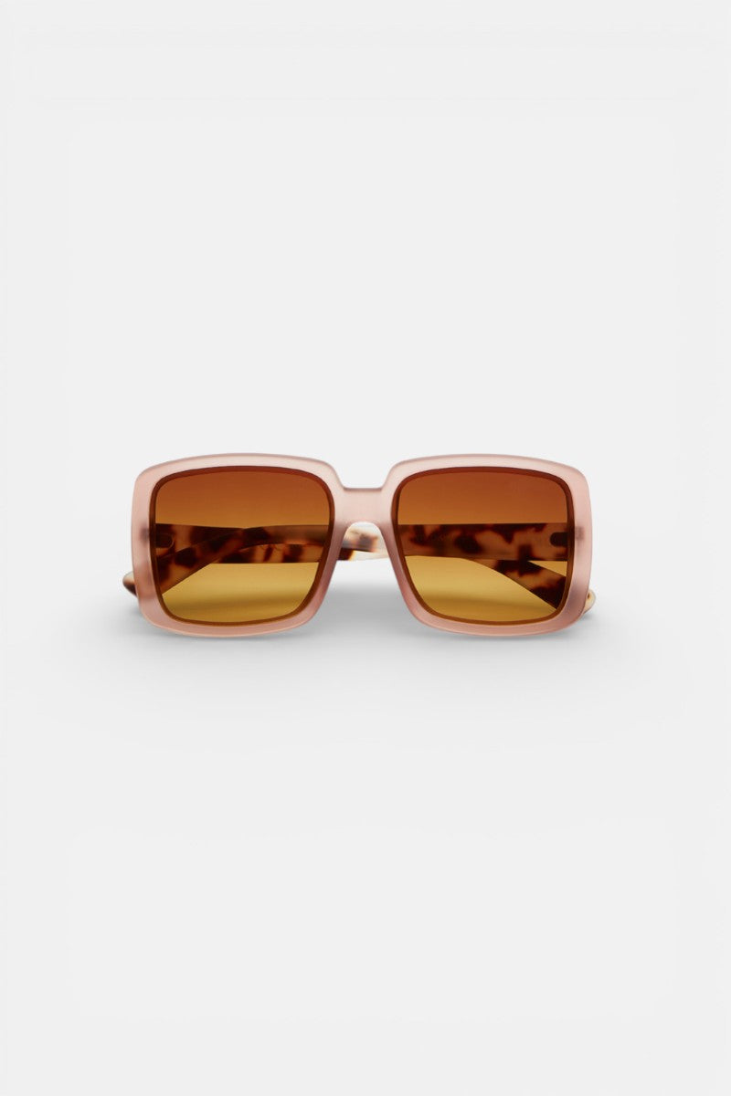 Okkia Oversize-Sonnenbrille mit quadratischem, dickem hellrosa Rahmen und amberfarbenen Gläsern (UV 400). Schildpatt-Muster auf der Innenseite der Bügel. Frontalansicht vor weißem Hintergrund.