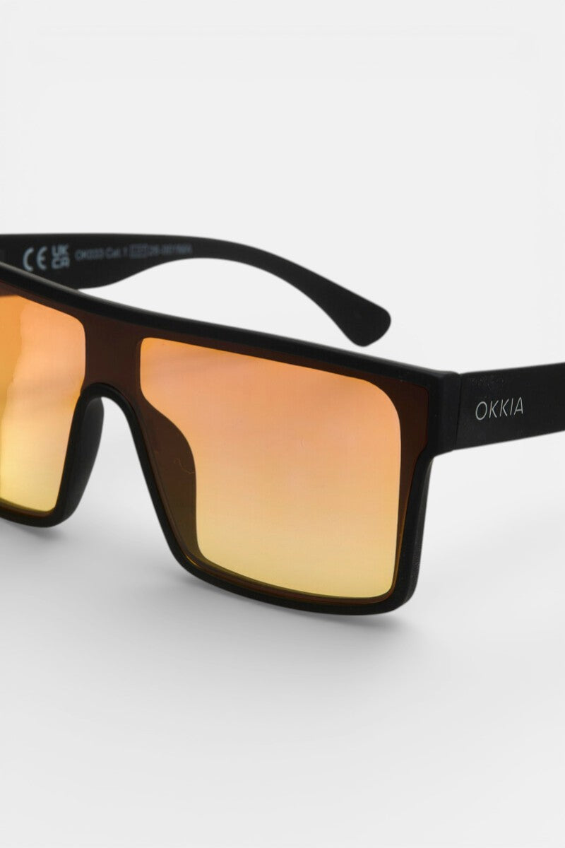 Nahaufnahme einer schwarzen, rechteckigen Sonnenbrille von Okkia mit breiten orange-verspiegelten Gläsern (UV 400 Schutz). Das weiße Okkia-Logo ziert den rechten Bügel. Das moderne Oversize-Design hebt sich vor weißem Hintergrund ab.