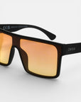 Nahaufnahme einer schwarzen, rechteckigen Sonnenbrille von Okkia mit breiten orange-verspiegelten Gläsern (UV 400 Schutz). Das weiße Okkia-Logo ziert den rechten Bügel. Das moderne Oversize-Design hebt sich vor weißem Hintergrund ab.