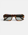 Rechteckige Sonnenbrille im Schildpatt-Look mit dickem, glänzendem Rahmen aus der Okkia STROMBOLI-Kollektion. Die dunklen, leicht verspiegelten Gläser erinnern an den Vintage-Look einer Sonnenbrille. Vor einem schlichten weißen Hintergrund bildet die Sonnenbrille den Blickfang des Bildes, wobei sich die Bügel seitlich nach außen erstrecken.