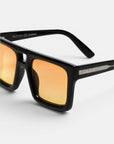 Nahaufnahme der Okkia VULCANO Sonnenbrille: schwarze, rechteckige Sonnenbrille mit goldverspiegelten Gläsern. Der glänzende Rahmen unterstreicht das moderne Design, während der Schriftzug „Okkia“ in Weiß auf den mattierten Bügeln eingraviert ist. Ein hellgrauer Hintergrund hebt das Bild hervor, wobei ein Teil der Innenseite des Bügels und Produktdetails sichtbar sind, was die übergroßen Proportionen dieses stilvollen Accessoires unterstreicht.