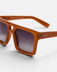 Nahaufnahme einer orangefarbenen, rechteckigen Okkia VULCANO Sonnenbrille mit übergroßem, breitem Rahmen und grauen Verlaufsgläsern. Der Markenname „Okkia“ ist in Weiß auf dem linken Bügel aufgedruckt. Vor einem schlichten, hellen Hintergrund hebt das Bild das moderne Design und die stilvolle Ausstrahlung der Sonnenbrille hervor.