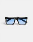 Rechteckige Okkia VULCANO Sonnenbrille mit dickem, schwarz-transparentem Rahmen und blau getönten Gläsern, abgebildet in Frontalansicht vor einem schlichten weißen Hintergrund. Das moderne Design zeichnet sich durch Oversize-Proportionen und Gläser mit Farbverlauf aus, der von tiefem zu hellem Blau übergeht.