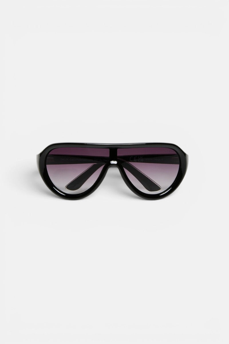 Eine schwarze Oversize-Pilotenbrille von Okkia wird auf weißem Hintergrund nach vorne gerichtet präsentiert. Sie zeichnet sich durch einen breiten Rahmen und dunkle Verlaufsgläser aus. Die Bügel der Sonnenbrille sind nach innen geklappt, was ihr ein modernes und markantes Design mit minimalistischem Charme verleiht. Diese PANAREA-Sonnenbrille verfügt über polarisierte Gläser von Okkia, die für verbesserte Sichtklarheit und Schutz sorgen.