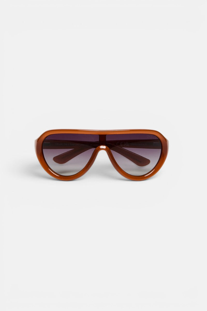 Braune, oval geformte Okkia PANAREA-Sonnenbrille mit einem breiten Kunststoffrahmen, dunkel getönten Gläsern und breiten Bügeln. Dieses moderne und sportliche Modeaccessoire ist vor einem schlichten weißen Hintergrund nach vorne gerichtet abgebildet.
