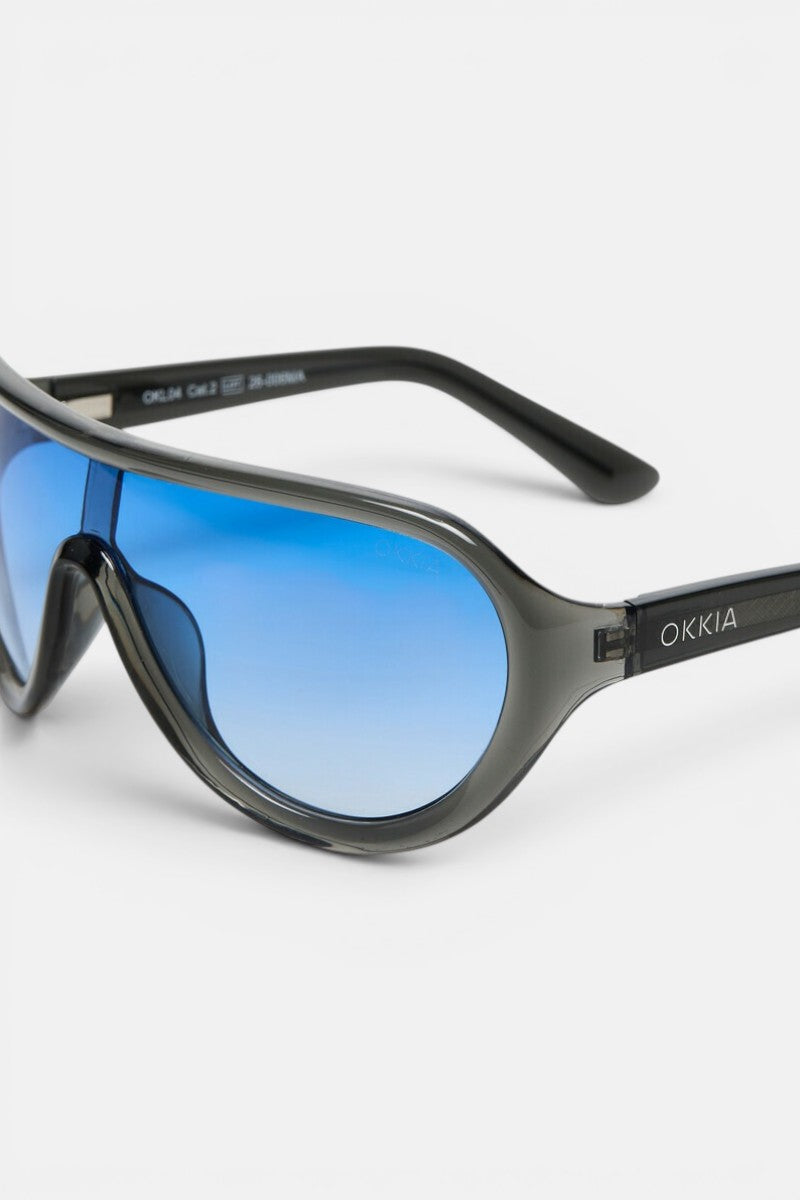 Nahaufnahme einer sportlichen Sonnenbrille mit schwarzem Rahmen und blauen, polarisierten Gläsern mit Farbverlauf. Der Markenname „Okkia“ ist in Weiß auf dem Bügel zu sehen. Vor einem schlichten weißen Hintergrund hebt das Bild das moderne, geschwungene Design und die reflektierenden Eigenschaften der Gläser hervor – was diese auffällige Brille zu einem idealen Modeaccessoire macht.