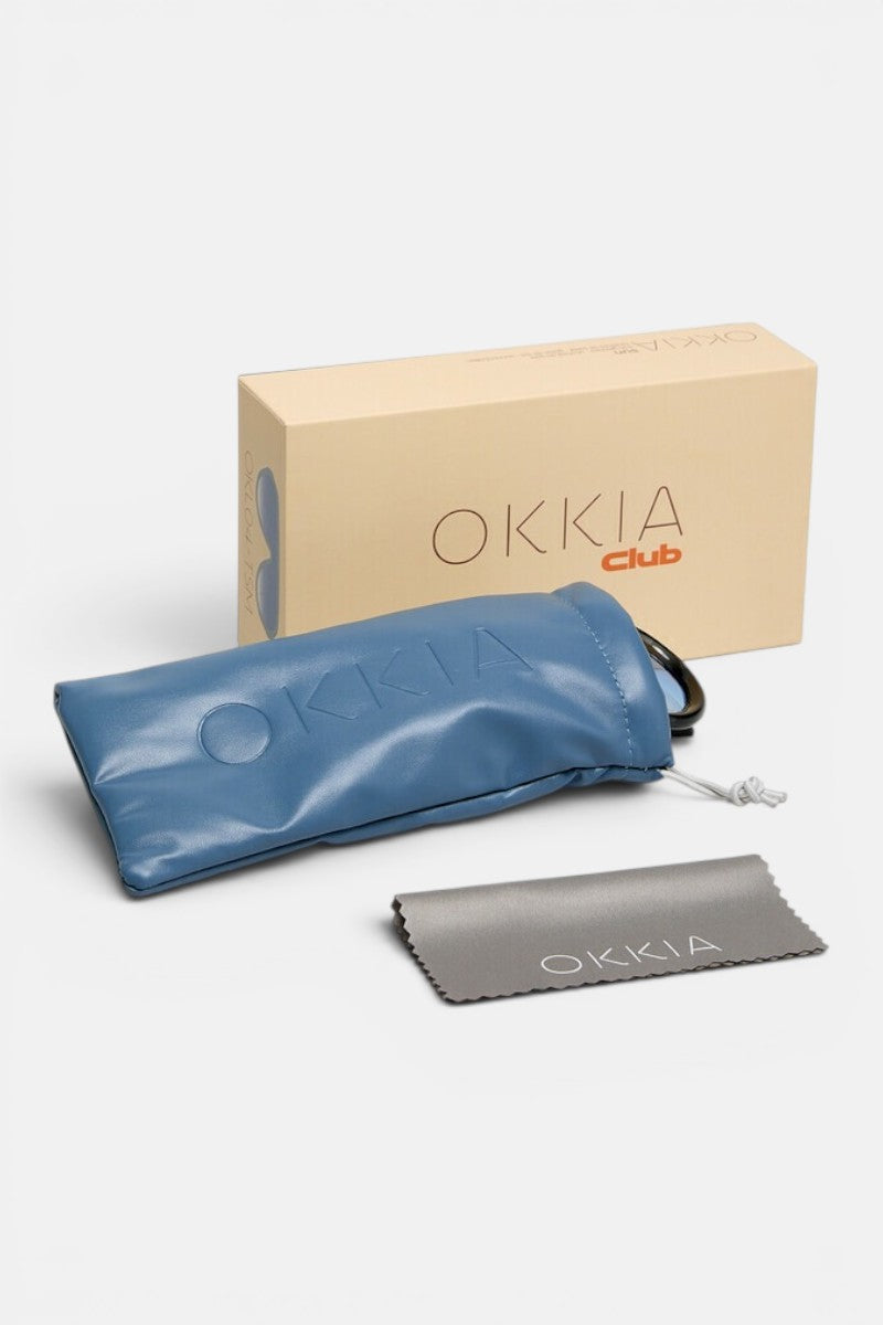 Auf einer weißen Fläche sind eine beigefarbene Okkia Club-Box, ein blauer, weicher Beutel mit geprägtem Okkia-Logo und Kordelzugverschluss sowie ein graues Reinigungstuch mit dem Aufdruck „Okkia“ angeordnet. Ideal zur sicheren Aufbewahrung Ihrer Okkia-Brille oder Ihres Modeaccessoires mit polarisierten Gläsern – alle Artikel sind übersichtlich präsentiert.
