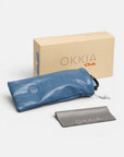 Auf einer weißen Fläche sind eine beigefarbene Okkia Club-Box, ein blauer, weicher Beutel mit geprägtem Okkia-Logo und Kordelzugverschluss sowie ein graues Reinigungstuch mit dem Aufdruck „Okkia“ angeordnet. Ideal zur sicheren Aufbewahrung Ihrer Okkia-Brille oder Ihres Modeaccessoires mit polarisierten Gläsern – alle Artikel sind übersichtlich präsentiert.