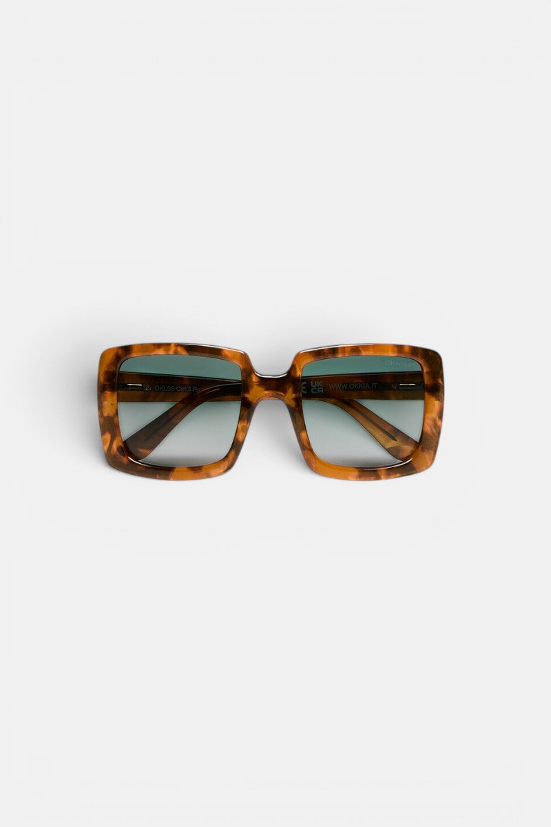 Eine quadratische Sonnenbrille mit einem breiten, braunen Schildpatt-Rahmen und dunklen, verlaufsgetönten Gläsern ist auf einem schlichten weißen Hintergrund zu sehen. Die Okkia CLUB Sonnenbrille besticht durch ein markantes, retro-inspiriertes Oversize-Design mit breiten Bügeln und polarisierten Gläsern, die sowohl Stil als auch optimalen Augenschutz bieten.