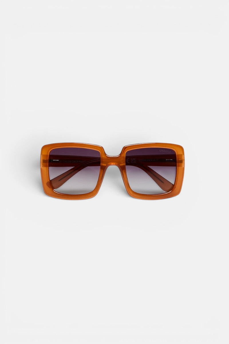 Quadratische Sonnenbrille von Okkia mit einem breiten, glänzenden, bernsteinbraunen Kunststoffrahmen und dunklen Verlaufsgläsern, präsentiert vor einem schlichten weißen Hintergrund. Die sichtbaren Scharniere an den Bügeln und die Frontansicht unterstreichen das symmetrische Oversize-Design. Diese ISCHIA-Sonnenbrille von Okkia ist zudem mit polarisierten Gläsern ausgestattet, die für verbesserte Sichtklarheit und hohen Tragekomfort sorgen.