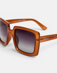 Nahaufnahme der Okkia ISCHIA Sonnenbrille mit einem markanten, quadratischen Rahmen in kräftigem, durchscheinendem Orange und dunklen Verlaufsglasgläsern. Das Modell im Oversize-Design trägt den weißen Okkia-Schriftzug auf dem Bügel. Die Sonnenbrille wird vor einem schlichten weißen Hintergrund präsentiert, um die Details besonders hervorzuheben.