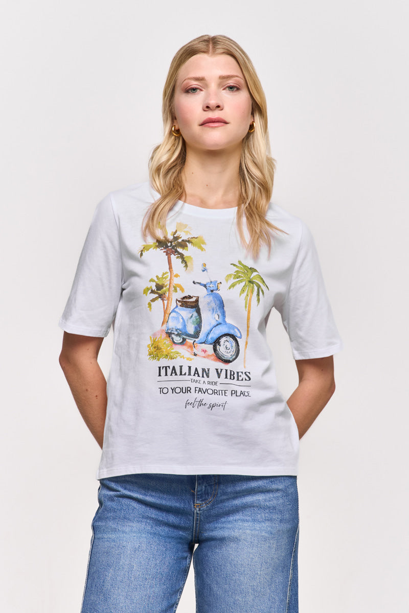 Eine blonde Frau trägt ein weißes Princess Goes Hollywood Baumwolle T-Shirt mit einem Vespa-Aufdruck, Palmen und "ITALIAN VIBES TO YOUR FAVORITE PLACE. feel the spirit". Sie posiert in hellblauen Jeans vor einem schlichten Hintergrund, die Hände in den Taschen.