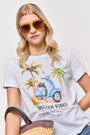 Eine blonde Frau mit brauner Sonnenbrille trägt ein weißes Baumwoll-T-Shirt von Princess Goes Hollywood mit einer Vespa, Palmen und dem Aufdruck "ITALIAN VIBES" und hält eine Strohtasche vor einem schlichten weißen Hintergrund.