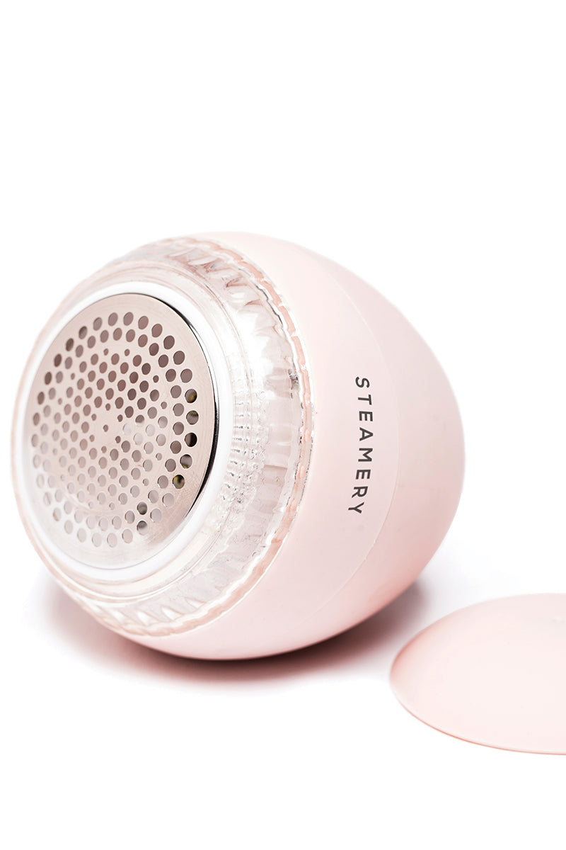 Nahaufnahme eines hellrosa Steamery-Rasierers mit rundem, perforiertem Metallkopf und klarem Kunststoffrand. Der Schriftzug "Steamery" ist senkrecht auf der Seite aufgedruckt. Die passende rosafarbene Kappe befindet sich in der Nähe auf einem weißen Hintergrund.