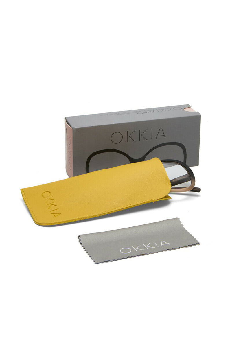 A pair of Okkia eyeglasses partially inside a yellow case is placed before a gray Okkia-branded box. A light gray cleaning cloth with the Okkia logo lies in front, all set against a white background.
