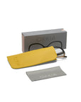 A pair of Okkia eyeglasses partially inside a yellow case is placed before a gray Okkia-branded box. A light gray cleaning cloth with the Okkia logo lies in front, all set against a white background.