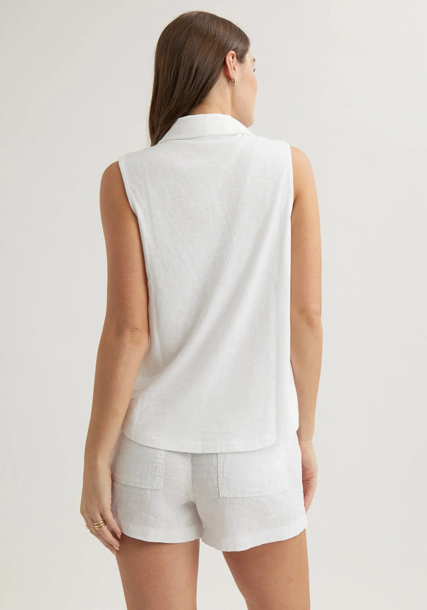 A woman with straight brown hair wears a Bella Dahl sleeveless cotton-blend top with a shirt collar and white linen shorts featuring visible back pockets, standing against an off-white background with her left arm relaxed at her side.