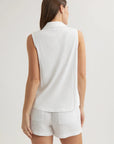 A woman with straight brown hair wears a Bella Dahl sleeveless cotton-blend top with a shirt collar and white linen shorts featuring visible back pockets, standing against an off-white background with her left arm relaxed at her side.